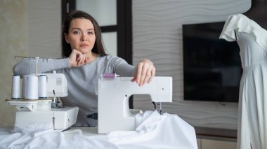 Genç beyaz kadın evde dikiş dikiyor.