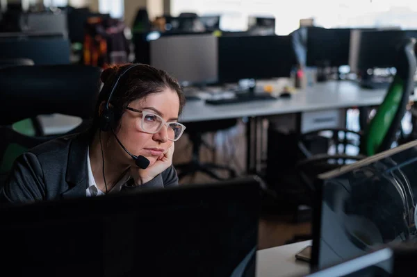 Unhappy woman in headset works overtime. Exhausted female call center operator in the office