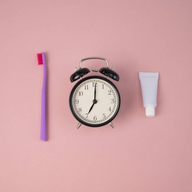 Diş fırçası, bir tüp diş macunu ve pembe arka planda çalar saat. Dişlerini fırçalama zamanı..