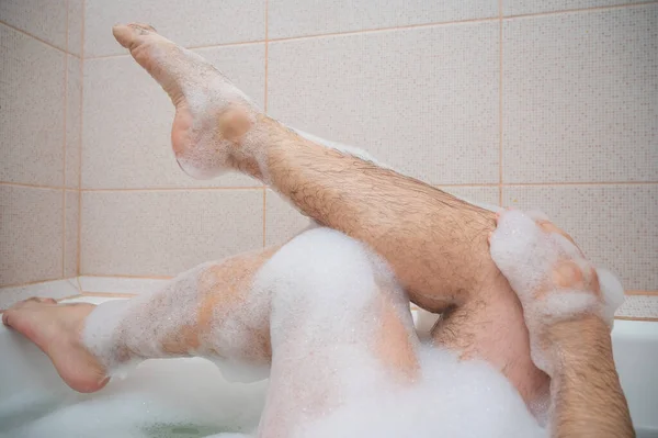 Funny picture of a man taking a relaxing bath. Close-up of male feet in a bubble bath. Top view
