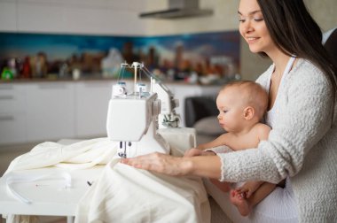 Genç bir kadın mutfakta dikiş dikiyor ve küçük bir çocuğu tutuyor. Annem küçük oğluna dikiş makinesi dikmeyi öğretiyor. Kendi kendini izole etme ödevi