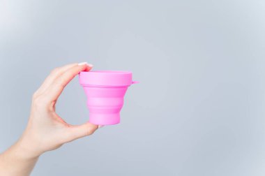 Beyaz arka planda adet bardağını sterilize etmek için plastik bardak tutan kadın. Temizlik için uygun bir konteynır