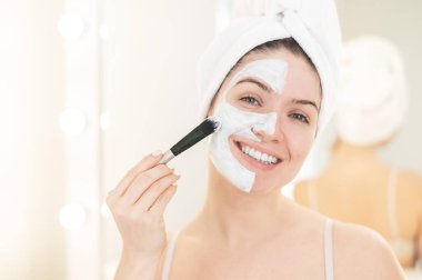 Saçında havlu olan güzel beyaz kadın kilden bir maske takıyor. Evdeki güzellikle ilgilenmek.