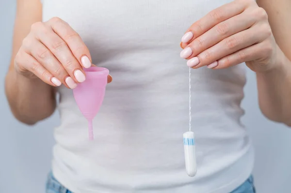 Close-up de uma mulher segurando um copo menstrual rosa e tampão contra um fundo branco — Fotografia de Stock