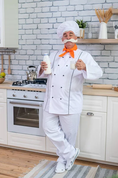 Un laitier âgé boit du lait de vache dans la cuisine. — Photo