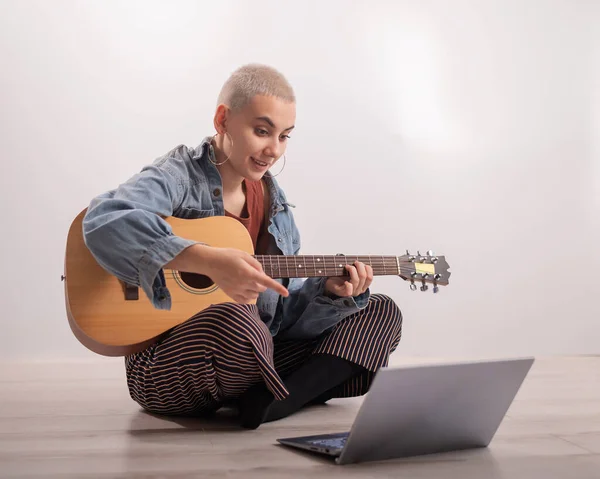 Jonge hippe vrouw die thuis op de vloer zit en gitaarles kijkt op laptop. Muziek voor afstandsonderwijs in quarantaine — Stockfoto