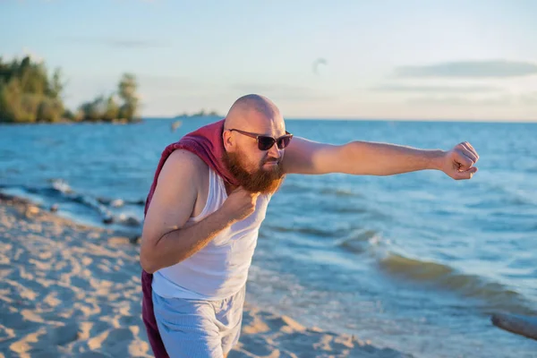 Un uomo brutale che posa sulla spiaggia imitando un supereroe volante. — Foto Stock