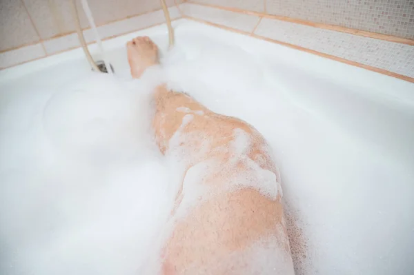 Close-up de pernas peludas masculinas em espuma. Um homem sem rosto está tomando um banho relaxante — Fotografia de Stock