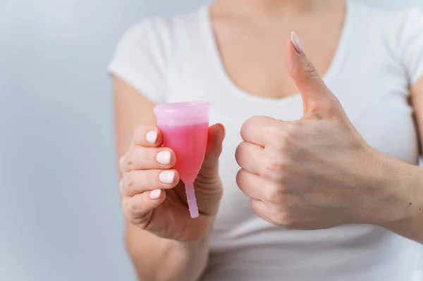 Una donna senza volto che indossa una t-shirt bianca tiene una tazza mestruale rosa con liquido rosso all'interno — Foto Stock