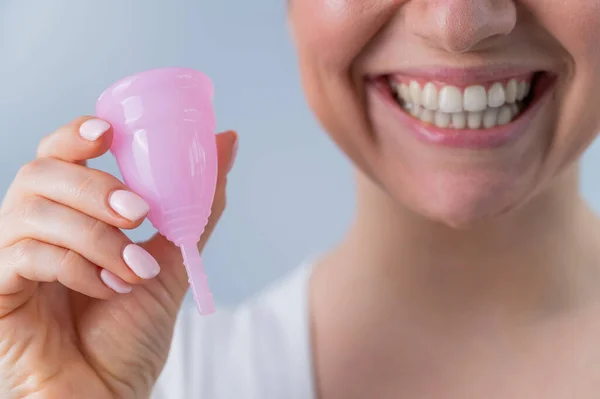 Retrato de cerca de una mujer caucásica sonriente sosteniendo una copa menstrual rosa sobre fondo blanco. Alternativa a tampones y almohadillas en días críticos. — Foto de Stock