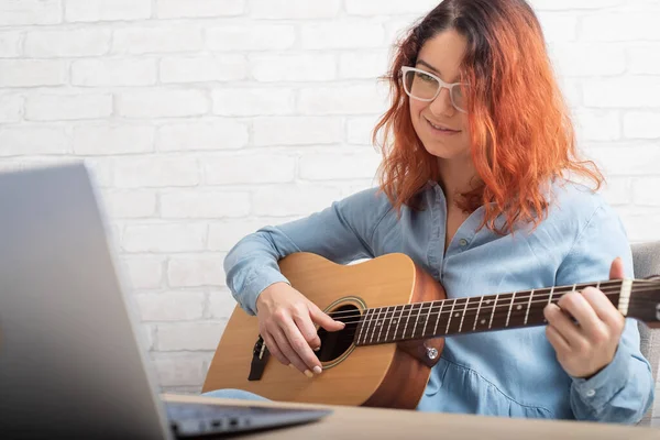 Een vrouw leert om online gitaar te spelen. Remote muzieklessen op een laptop — Stockfoto