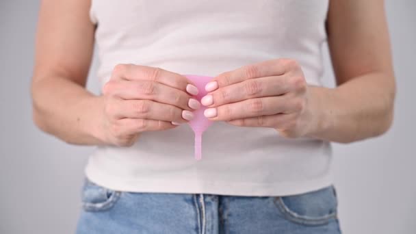 Una mujer sin rostro sostiene una copa menstrual rosa doblada. Alternativa a los tompones y almohadillas — Vídeos de Stock