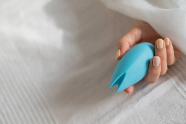 Kobieta bez twarzy leży w łóżku pod kocem trzymając wibrator łechtaczkowy. Dziewczyna masturbuje się — Zdjęcie stockowe
