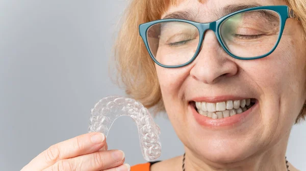 Uma mulher idosa feliz veste aparelhos removíveis transparentes. Odontologia cosmética para todas as idades — Fotografia de Stock