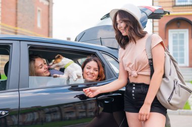 Üç kız arkadaş bir köpekle bir arabada seyahat ediyorlar. İki kadın arka koltukta Jack Russell Terrier 'la oturuyor ve pencereden dışarı bakıyor. Üçüncüsü ise yakınlarda duruyor.