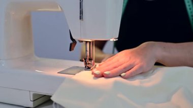 Yakın plan. Bir kadın evde elektrikli dikiş makinesinde çalışıyor.