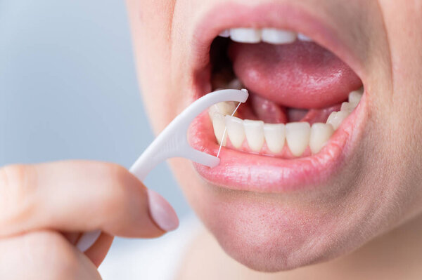 Caucasian woman brushing teeth with toothpick with dental floss on white background.