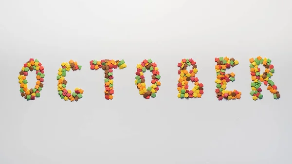 Oktober inscriptie op een witte achtergrond. Hagelslag in de vorm van veelkleurige esdoornbladeren — Stockfoto