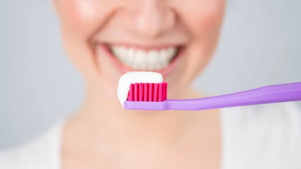 Uma mulher com um sorriso branco-neve segura uma escova de dentes com pasta em um fundo branco — Fotografia de Stock