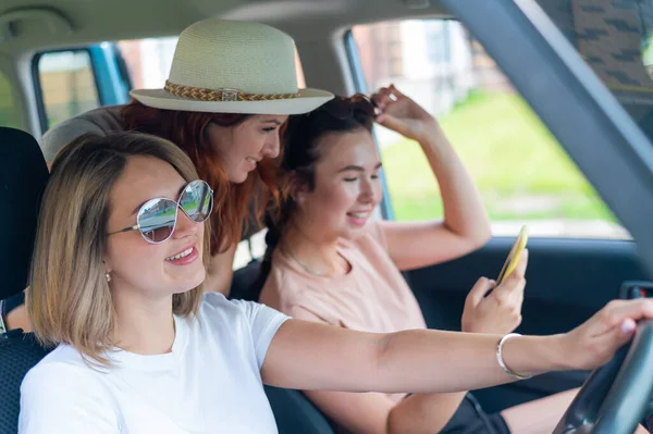 Três namoradas felizes fazem uma viagem. Mulheres Andar de carro, olhar para o telefone e rir. — Fotografia de Stock