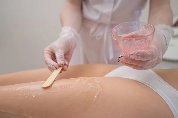 El maestro aplica el gel anestésico con una espátula a las piernas de las mujeres antes de la depilación láser. Depilación permanente con un dispositivo en la clínica — Foto de Stock