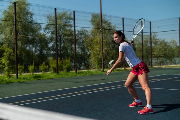 Νεαρή καυκάσια που παίζει τένις σε υπαίθριο γήπεδο μια ζεστή καλοκαιρινή μέρα. — Φωτογραφία Αρχείου