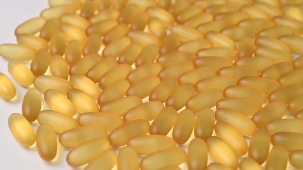 Átlátszó sárga kapszulák közelsége egy forgó fehér asztalon. Omega 3-at és halolajat tartalmazó étrend-kiegészítők — Stock videók