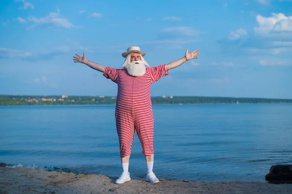 Un anziano uomo barbuto in un classico abito a righe e un cappello da barca gode di una passeggiata sulla spiaggia — Foto Stock