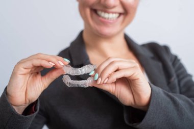Bir kadın şeffaf plastik bir ağız koruyucusu tutuyor. Ortodontistler diş düzeltme aygıtını ısırırlar