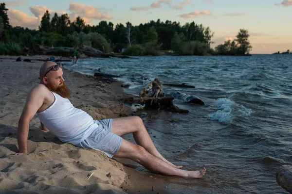 Divertente uomo calvo con la barba rossa vestita in biancheria intima in posa sulla spiaggia. Una parodia maschile divertente di una ragazza glamour. — Foto Stock