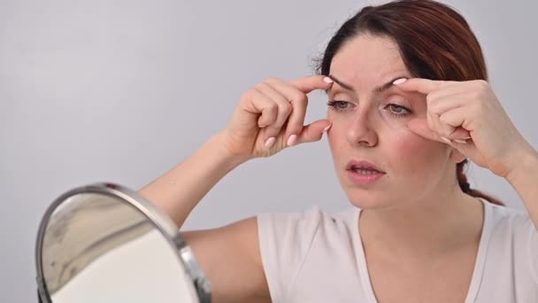 Vit kvinna ser sig själv i spegeln och är upprörd på grund av ansiktsrynkor i ansiktet. — Stockvideo