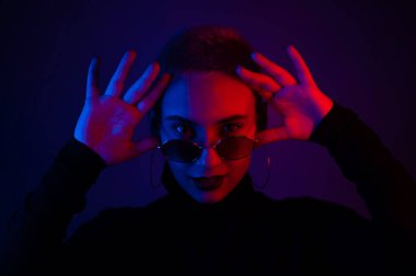 Güneş gözlüklü, kısa saçlı, neon ışıklı güzel bir kadının portresi.