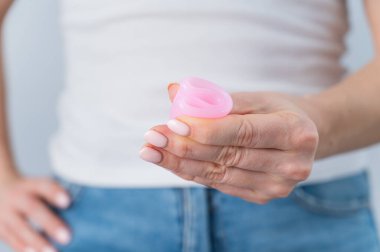 Yüzü olmayan bir kadın pembe bir adet kupası tutuyor. Tompon ve pedlere alternatif