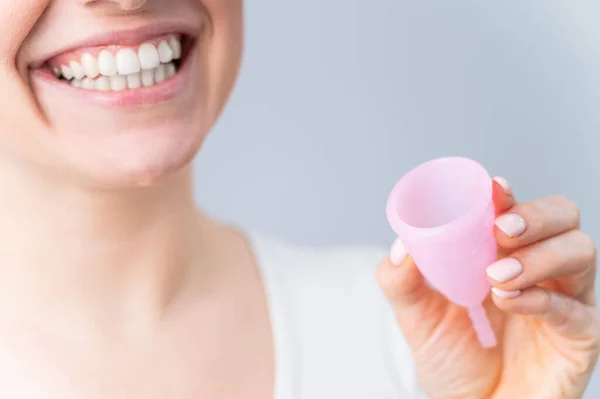 Close-up portret van een glimlachende blanke vrouw met roze menstruatiecup op witte achtergrond. Alternatief voor tampons en pads op kritieke dagen. — Stockfoto
