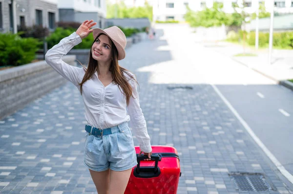 Mooie Kaukasische brunette vrouw in een hoed poseren met een koffer op een stad straat. — Stockfoto