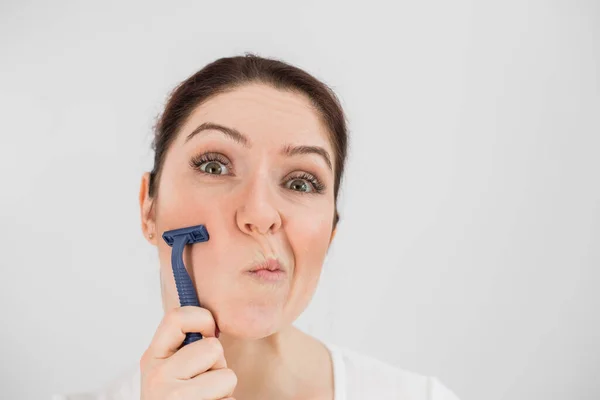 Mujer divertida caucásica se afeita la cara con una navaja de afeitar sobre un fondo blanco. Copiar espacio. — Foto de Stock