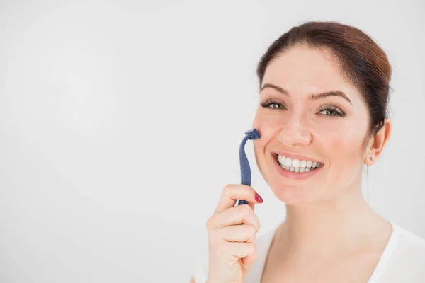 Mujer caucásica sonriente se afeita la cara con una navaja de afeitar sobre fondo blanco. Espacio vacío. — Foto de Stock