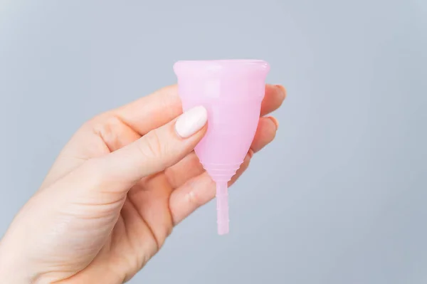 Großaufnahme einer weiblichen Hand mit einer rosa Menstruationstasse auf weißem Hintergrund. Sorge für die Umwelt. Umweltfreundliches weibliches Intimhygieneprodukt. — Stockfoto