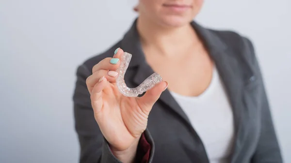 Una mujer sostiene un protector bucal de plástico transparente. Ortodoncistas dispositivo corrector de mordida — Foto de Stock