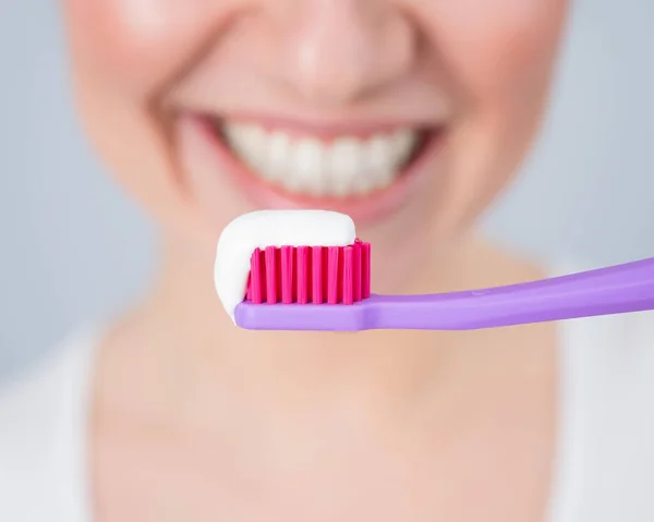 Una donna con un sorriso bianco come la neve tiene uno spazzolino da denti con pasta su uno sfondo bianco — Foto Stock