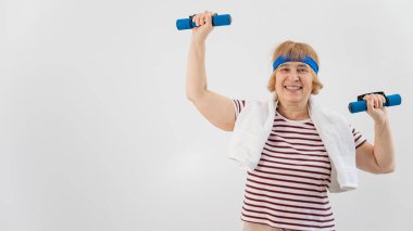 Kafasında mavi bandajlı yaşlı bir kadın beyaz arka planda dambıllarla trenlere biniyor.