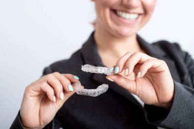 Bir kadın şeffaf plastik bir ağız koruyucusu tutuyor. Ortodontistler diş düzeltme aygıtını ısırırlar