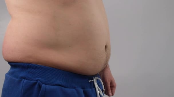 Close-up de uma barriga gorda masculina tremendo contra um fundo branco. Um homem obeso está dançando com um tronco nu — Vídeo de Stock