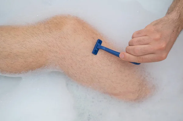 한 남자가 편안 한 목욕을 하고 다리를 면도 하고 있는 이상 한 그림입니다. 거품 목욕을 하고 있는 남성 발의 근접 사진. 위에서 본 풍경. — 스톡 사진