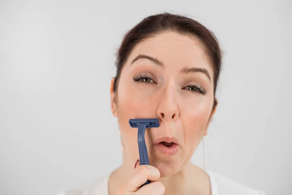 Mujer divertida caucásica se afeita la cara con una navaja de afeitar sobre un fondo blanco. Copiar espacio. — Foto de Stock