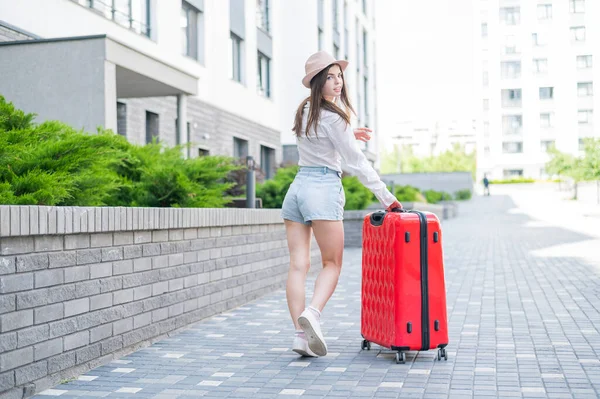 Mooie Kaukasische brunette vrouw in een hoed poseren met een koffer op een stad straat. — Stockfoto