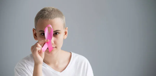 Ung kvinna med kort hår bär en vit t-shirt med ett rosa band som en symbol för bröstcancer på en vit bakgrund. — Stockfoto