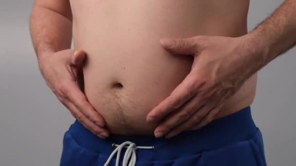 Närbild av en manlig fett skakande mage mot en vit bakgrund. Den feta mannen rör vid magen och visar tummen ner — Stockvideo