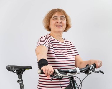 Beyaz arka planda bisiklet süren yaşlı beyaz bir kadın..