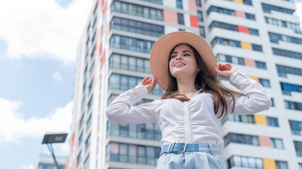 Feliz mujer joven caucásica en un sombrero y pantalones cortos camina en una calle de la ciudad en un día caluroso de verano —  Fotos de Stock